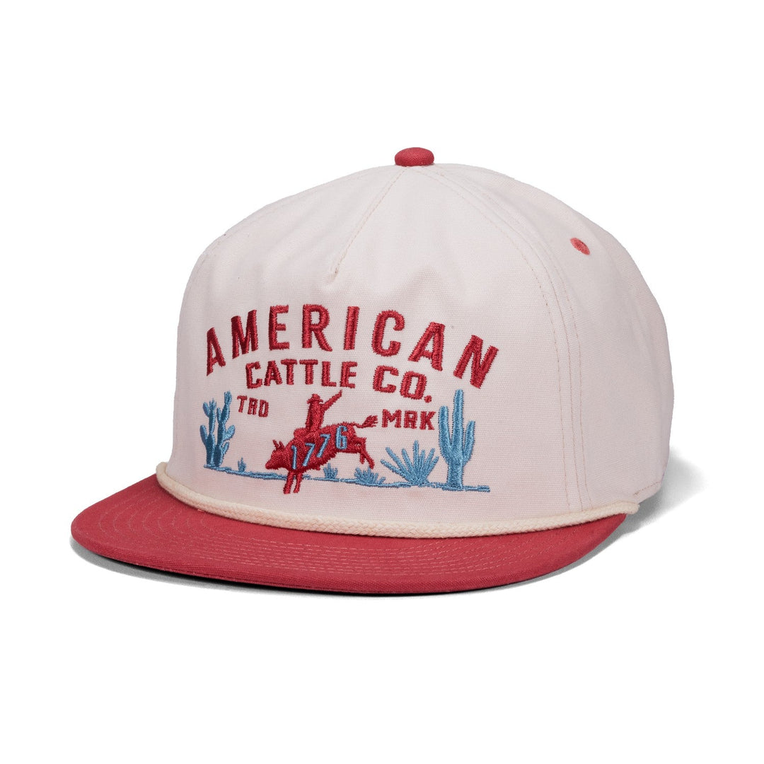 Show off your desert grit with the 8-Second Canvas snapback in cream and red, featuring “American Cattle Co.” embroidery on the front, a red cowboy riding a bucking horse, and blue cactus graphics in the background.