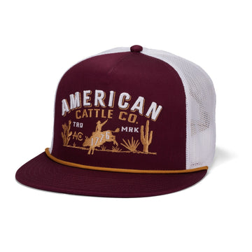 Introducing the 8-Second Hat by Rural Cloth—a maroon and white mesh trucker snapback featuring a flatbill profile. "American Cattle Co." is embroidered on the front above a striking design of a cowboy, horse, cacti, and "AC 1776." A gold cord detail across the flat bill adds an extra touch of style to this distinctive hat.