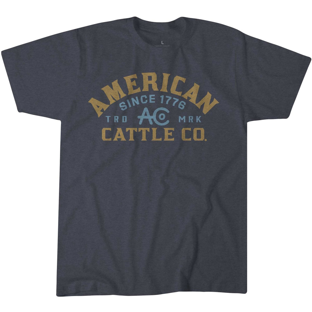 The Rural Cloth ACC Mark Tee is a comfortable Heather Navy shirt made of combed ring spun cotton, featuring "AMERICAN CATTLE CO. SINCE 1776 TRD MRK AC" printed in yellow and blue on the front.
