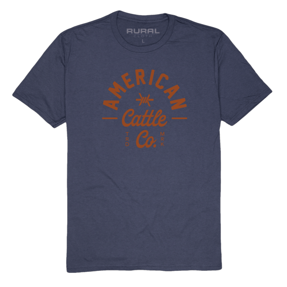 The Barb Tee by American Cattle Co is a navy premium cotton blend t-shirt with "American Cattle Co." in bold orange on the front and a subtle "Rural" print inside the neck—perfect for ranchers.