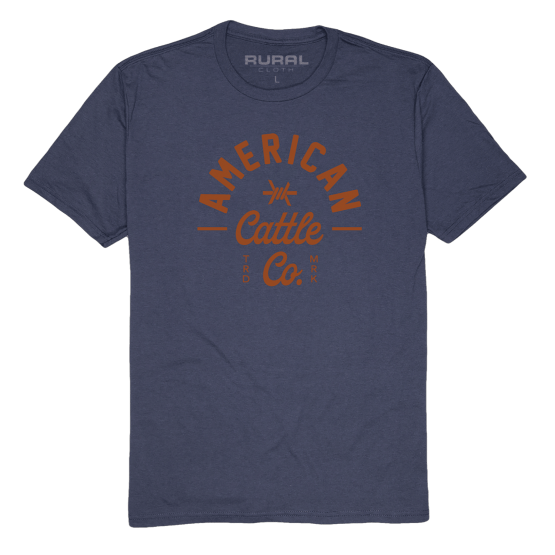 The Barb Tee by American Cattle Co is a navy premium cotton blend t-shirt with "American Cattle Co." in bold orange on the front and a subtle "Rural" print inside the neck—perfect for ranchers.