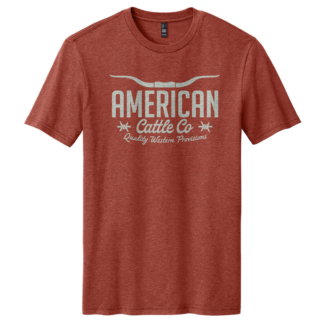 The Barbed Script Tee by American Cattle Co is a heathered red short-sleeve shirt with bold western "AMERICAN Cattle Co Quality Western Provisions" text and a striking white longhorn horns graphic on the chest.