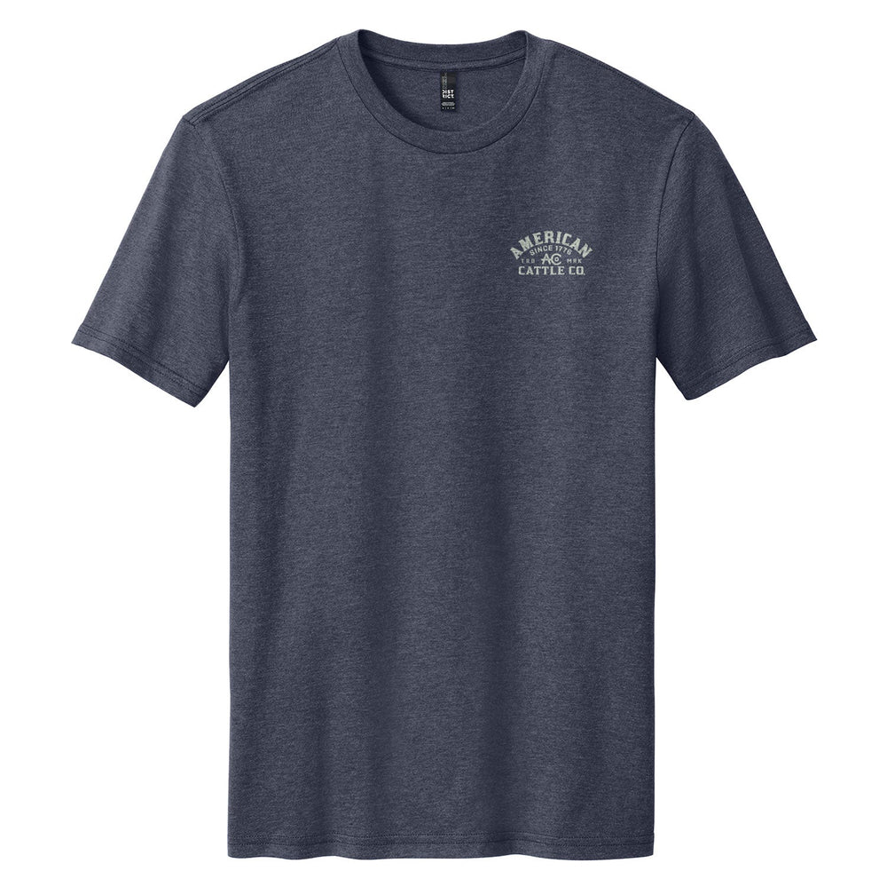 The Bucking Horse Tee by American Cattle Co is a plain, short-sleeved, dark gray vintage rodeo shirt featuring a small white "Merican Cattle Co" logo on the left chest, shown laid flat on a white background.