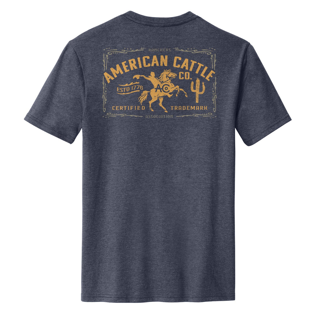 The Bucking Horse Tee by American Cattle Co is shown from the back in heathered navy, featuring a yellow graphic of a cowboy riding a bull with “American Cattle Co.” and vintage rodeo-inspired text styled like an old label.