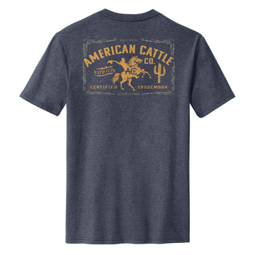 The Bucking Horse Tee by American Cattle Co is shown from the back in heathered navy, featuring a yellow graphic of a cowboy riding a bull with “American Cattle Co.” and vintage rodeo-inspired text styled like an old label.