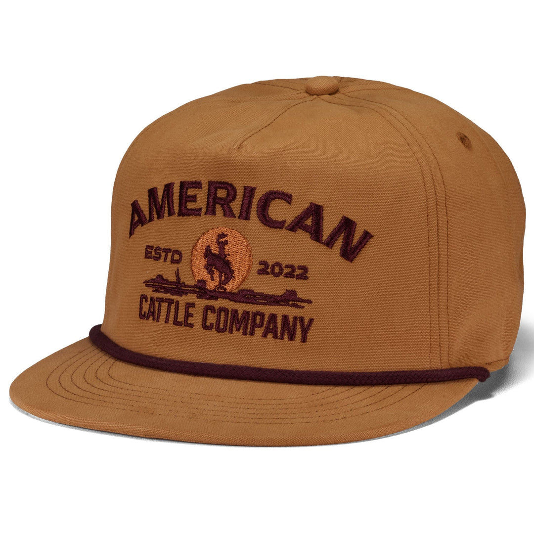 The American Cattle Co Cattle Company Hat is a brown snapback flat brim cap with "American Cattle Company ESTD 2022" and a bronc rider patch embroidered in dark brown, plus a decorative rope above the brim.