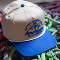The Rural Cloth Certified Ranchers Association Hat features beige and blue colors, 
