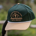 The Certified Ranchers Association Hat by Rural Cloth is a green and tan embroidered snapback with white trim, featuring the words 