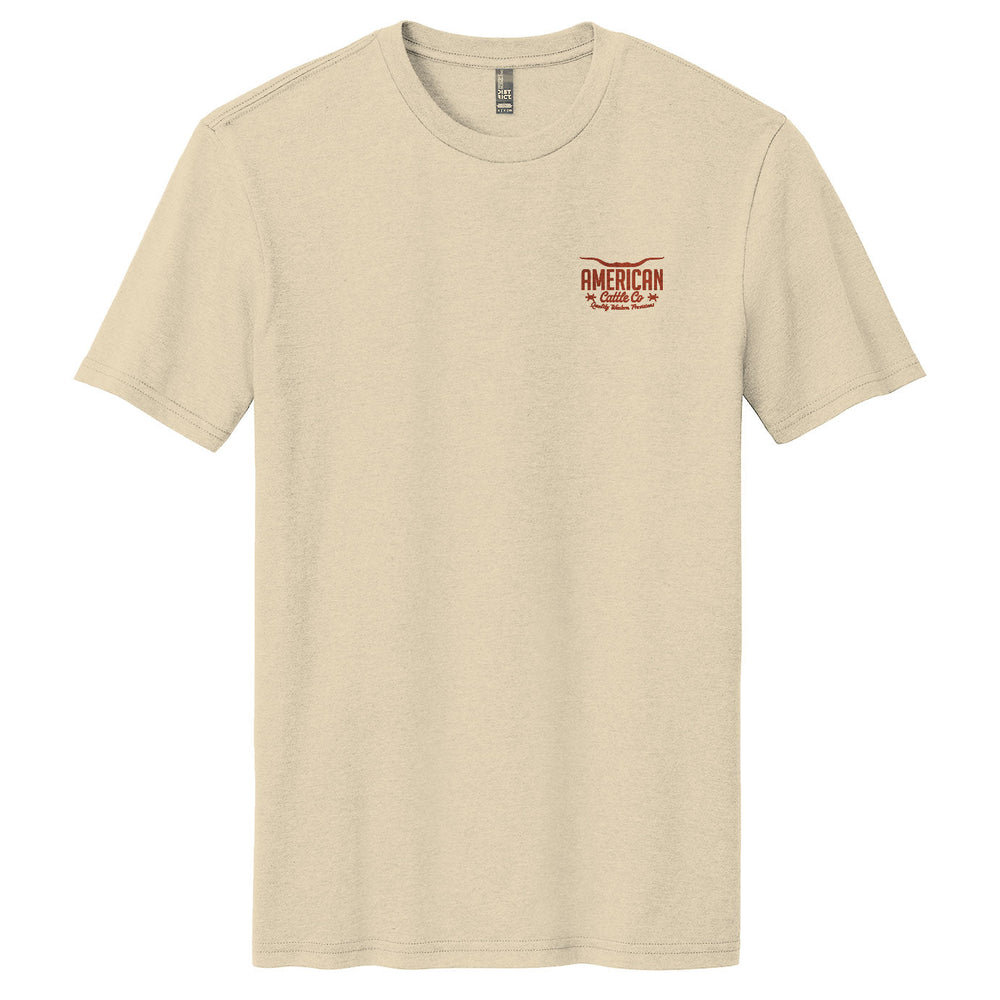 The Desert Longhorn Tee by American Cattle Co is a beige short-sleeve t-shirt with a small red and brown "AMERICAN Cattle Co." logo on the left chest, evoking classic cattle country style, shown on a plain white background.