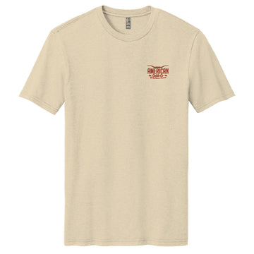 The Desert Longhorn Tee by American Cattle Co is a beige short-sleeve t-shirt with a small red and brown "AMERICAN Cattle Co." logo on the left chest, evoking classic cattle country style, shown on a plain white background.