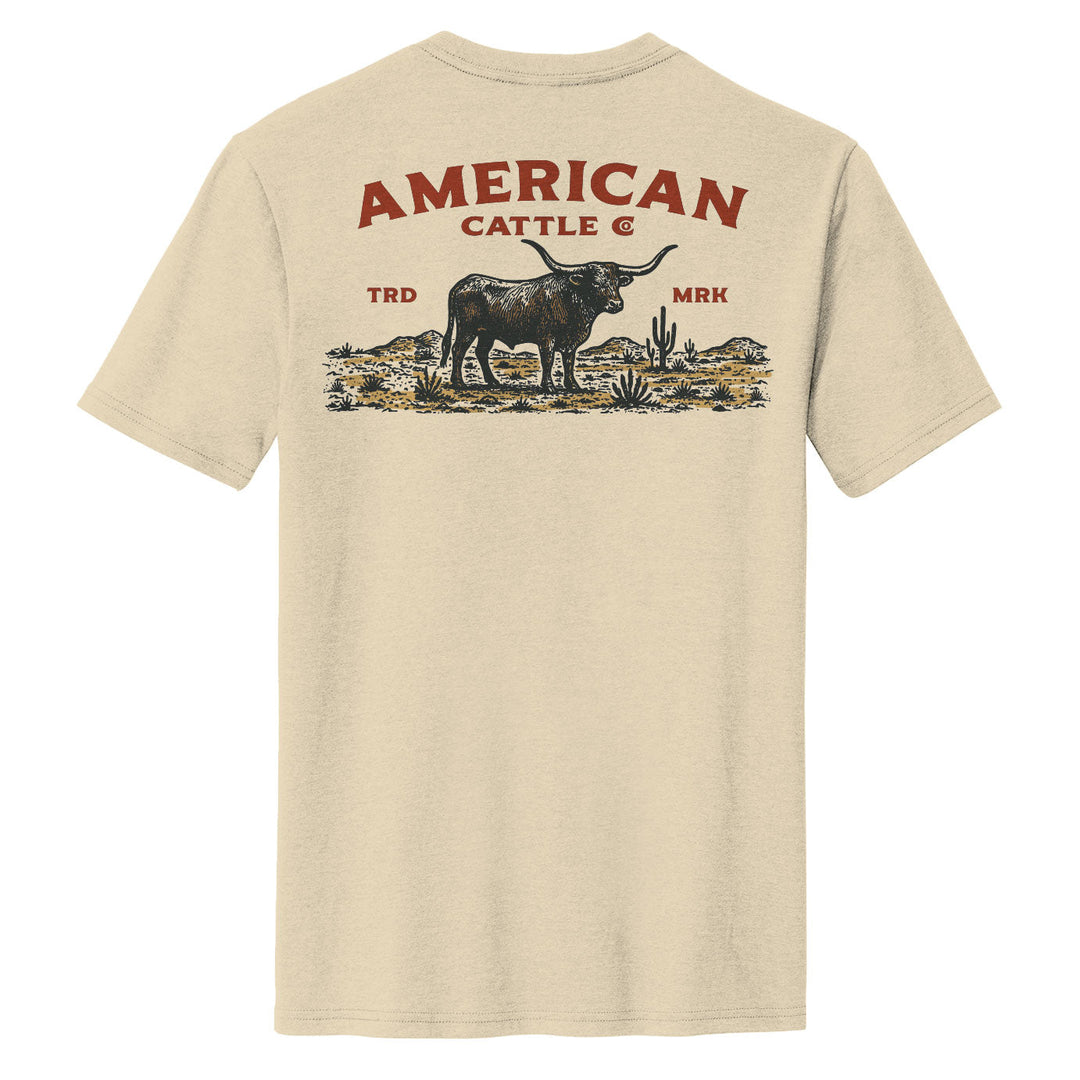 The American Cattle Co "Desert Longhorn Tee" is a beige shirt featuring a longhorn cow, cacti, and plants graphic on the back with bold red “AMERICAN CATTLE CO.” text above and “TRD” & “MRK” at the sides—a true Western desert style.