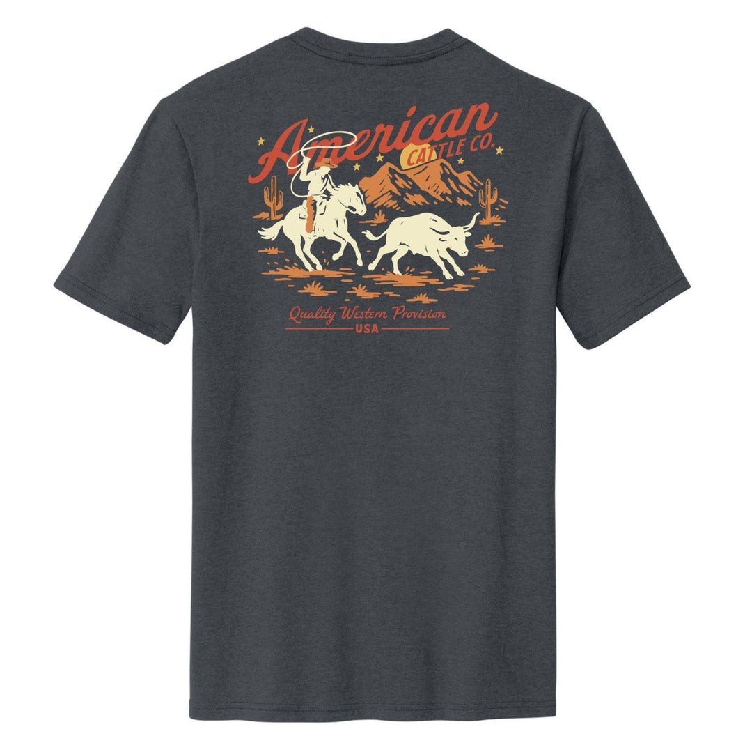The Frontier Tee by American Cattle Co is a dark gray shirt with a vintage western vibe, featuring a cowboy herding cattle, mountain and cactus graphics, and bold red-orange "American Cattle Co." and "Quality Western Provision USA" text.
