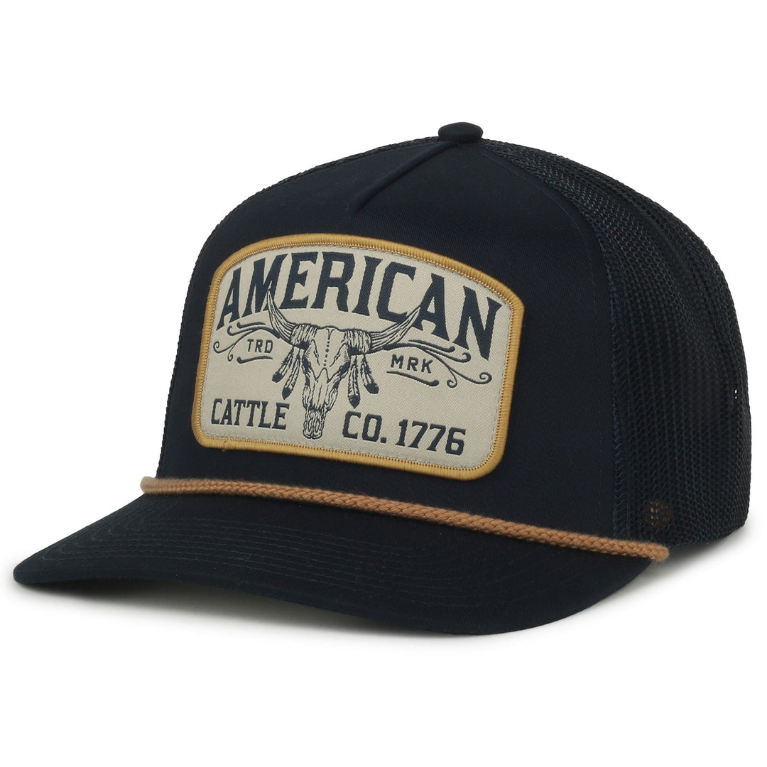 Navy mesh Headdress Hat by American Cattle Co with beige patch on front, "American Cattle Co. 1776" text, longhorn skull graphic, and a brown cord above the brim for classic American grit.