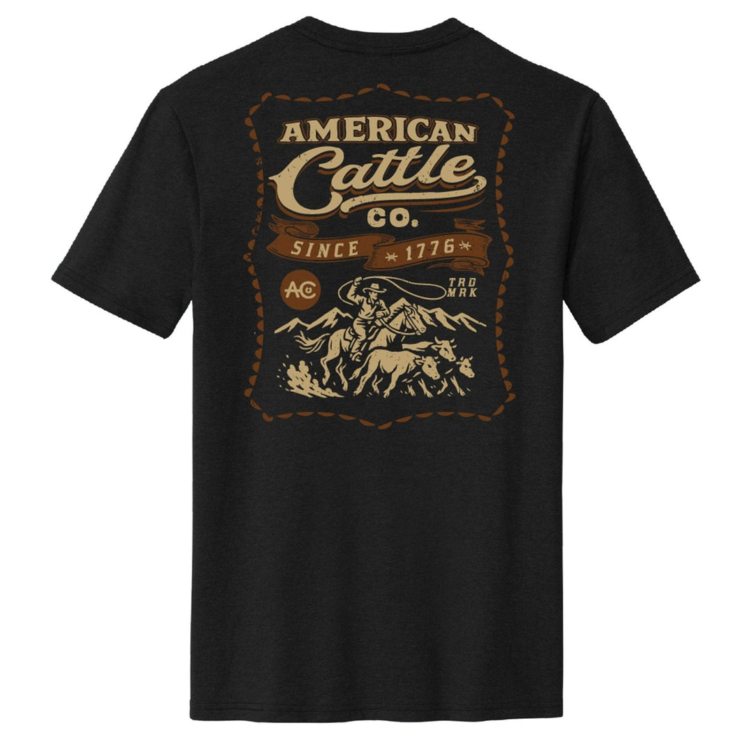 The American Cattle Co Heritage Tee is black with a large vintage "American Cattle Co. Since 1776" graphic and a beige-brown illustration of a cowboy herding cattle on the back.