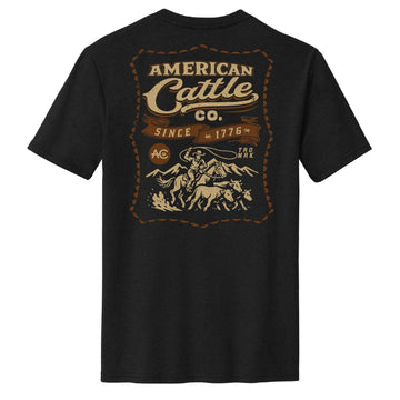 The American Cattle Co Heritage Tee is black with a large vintage "American Cattle Co. Since 1776" graphic and a beige-brown illustration of a cowboy herding cattle on the back.