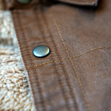 Metal snap, front placket and contrast stitching on the Homestead Jacket in Buck, with sherpa lining at the edge.