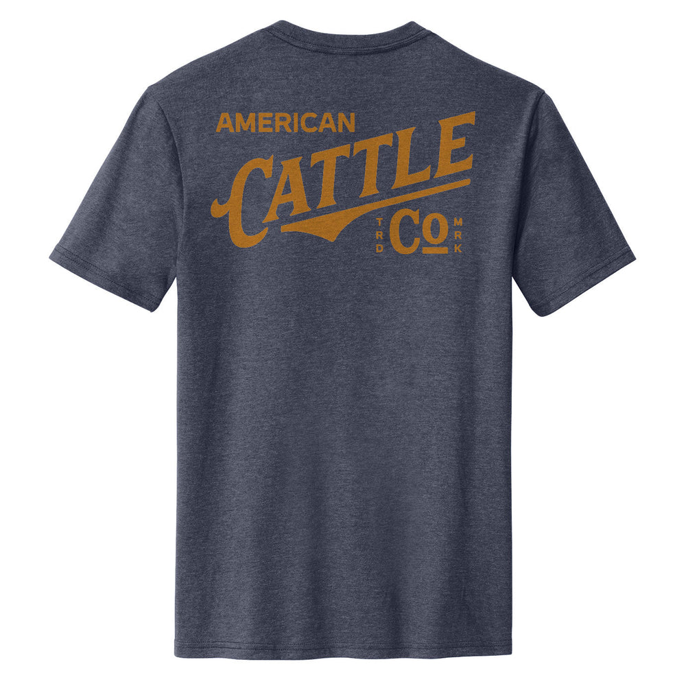 The Label Tee by American Cattle Co is shown from the back in heather navy, featuring large gold “AMERICAN CATTLE Co.” text with stylized lettering and small trademark symbols.