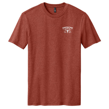 The Liberty Buck Tee by American Cattle Co is a heathered red western t-shirt featuring a small white "AMERICAN" graphic and two vintage cars on the left chest, shown laid flat on a white background.