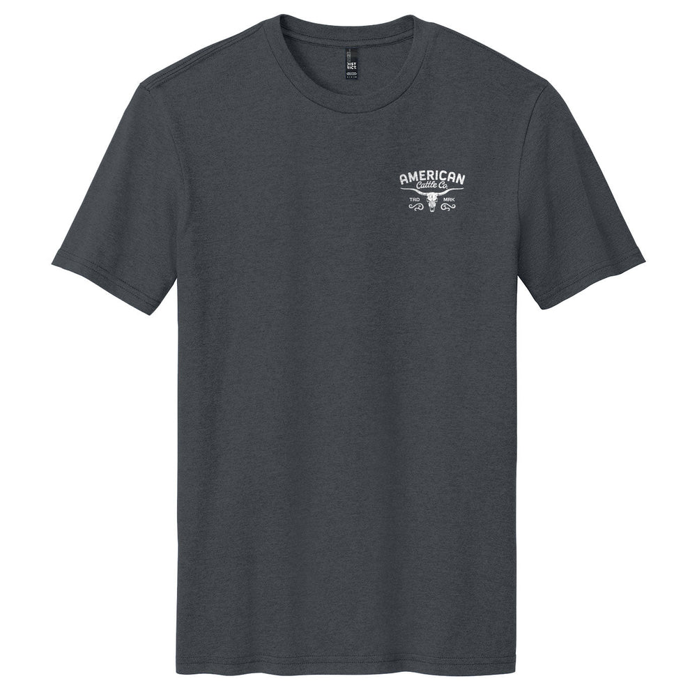 The Liberty Buck Tee by American Cattle Co is a plain dark gray western t-shirt with a small white "American Garage" text and crossed wrenches graphic on the left chest, designed in the classic American Cattle Co style.