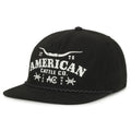 The Longhorn Barb Hat by Rural Cloth is a black snapback with a flat brim, featuring “American Cattle Co.” in white text, bull horn graphics, “1776,” and stylish decorative front accents.