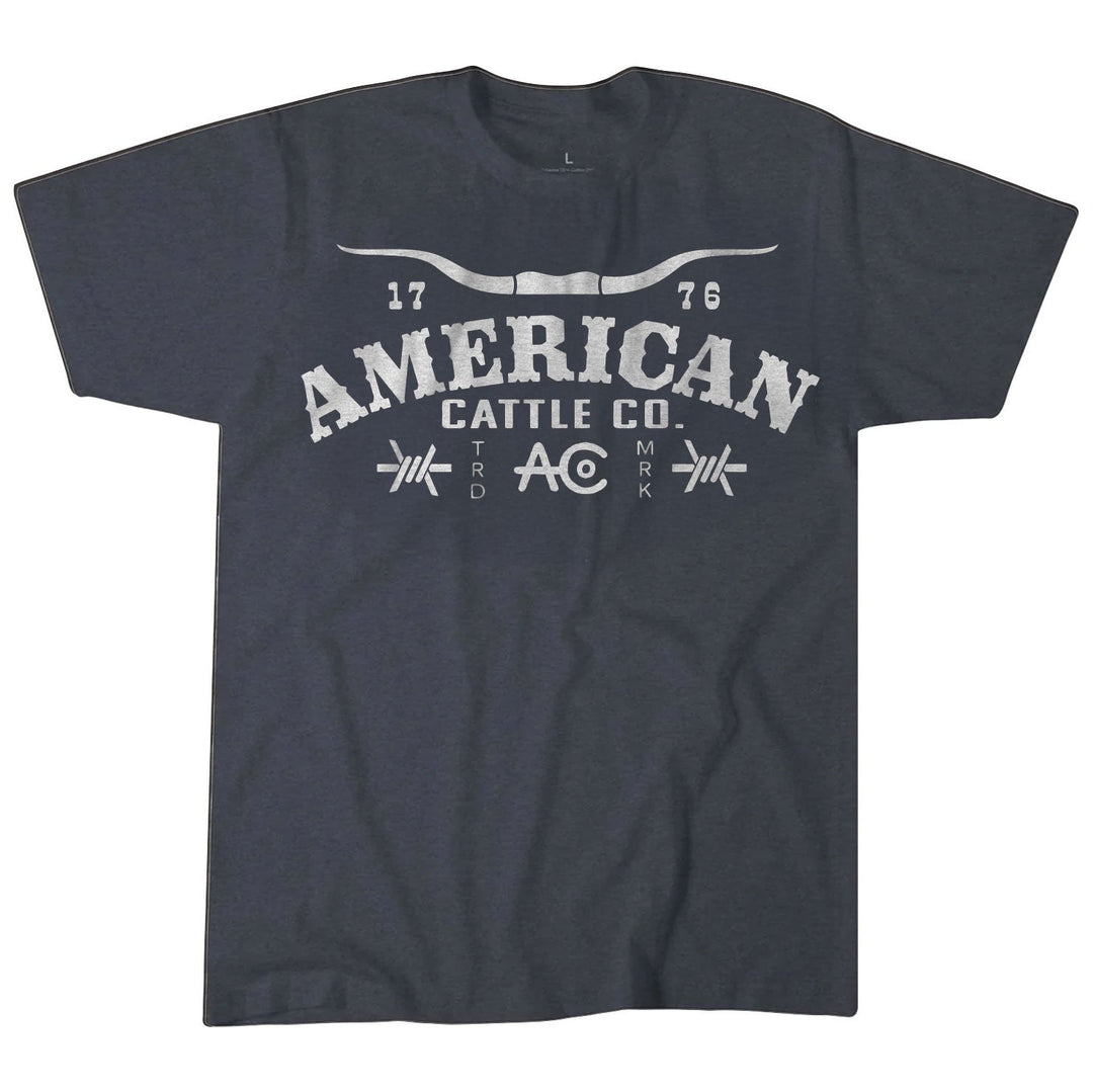 The Rural Cloth Longhorn Barb Tee in heather blue is crafted from a soft poly-cotton blend and features "AMERICAN CATTLE CO." in distressed white, flanked by "17" and "76," with a steer horn graphic—a classic Western-inspired tee.