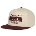The Longhorn Hat - Solid by Rural Cloth is a beige snapback with a maroon brim, top button, and front embroidery that reads 