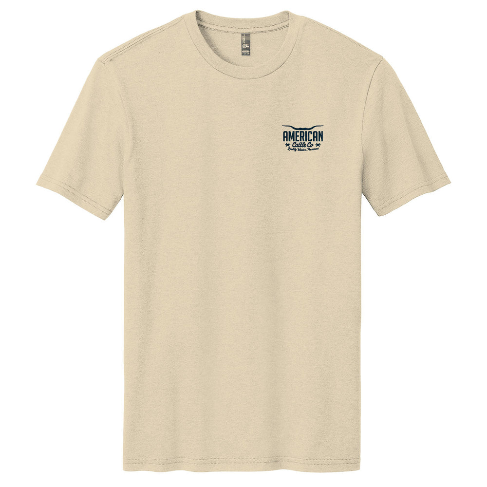 The American Cattle Co Quality Western Tee is a cream cotton blend with short sleeves, a classic crew neck, and a small "AMERICAN" logo on the left chest.