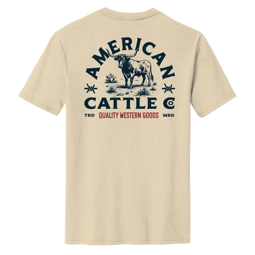 The Quality Western Tee by American Cattle Co features a cream cotton blend with a bold blue and red steer, desert plants, and “Quality Western Goods” print on the back—a perfect Western shirt for any wardrobe.