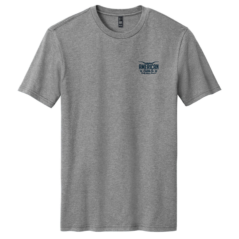 The American Cattle Co Range King Tee is a heather gray short-sleeve shirt with a small blue "American Road Trip" graphic on the left chest, shown laid flat on a white background.