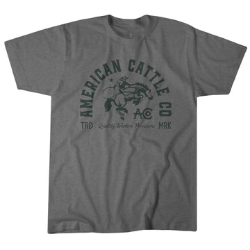 The Ride 'Em Cowboy Tee by American Cattle Co features a bold "American Cattle Co," "TRD," "Quality Western Provisions," and "MRK" print with a bucking horse and rider—ideal for fans of classic American cowboy style.