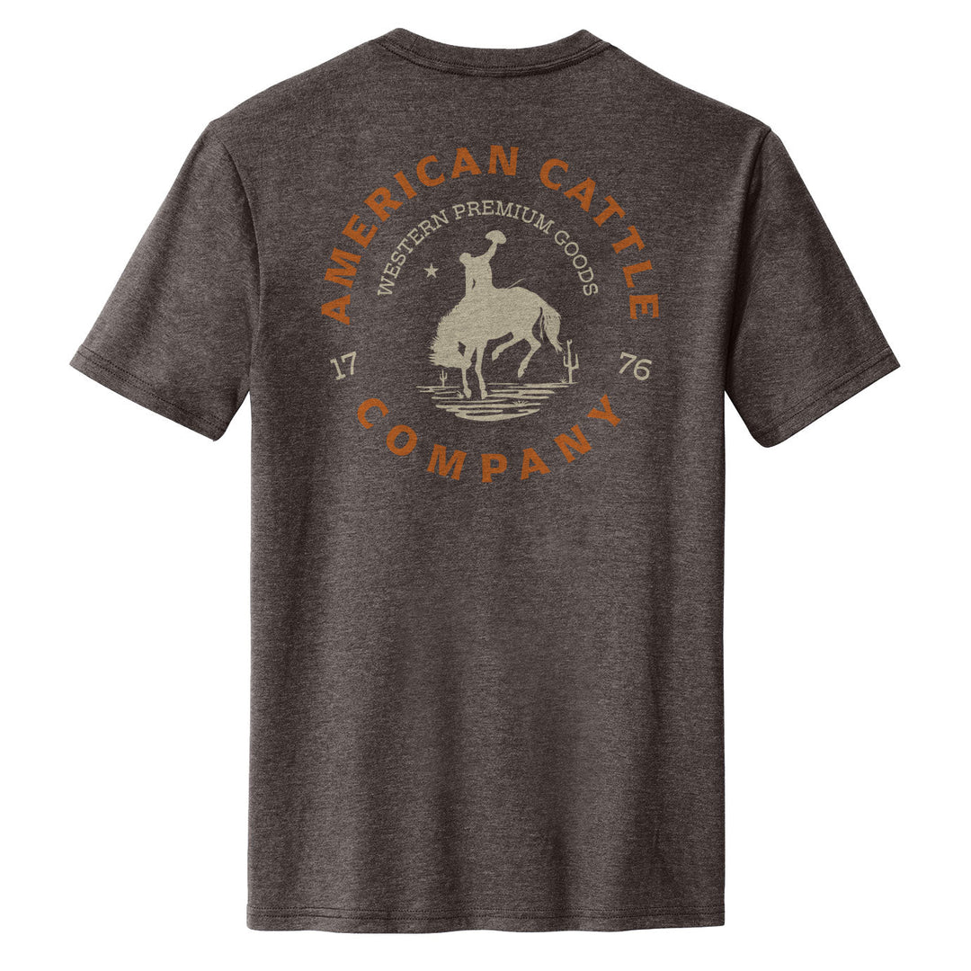 The Rodeo Star Tee by American Cattle Co is a heathered dark gray western shirt with a back graphic of a bronc rider atop a bucking bull, framed by "American Cattle Company," "Western Premium Goods," and "1776.