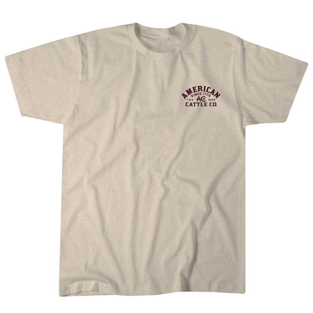 Introducing the Shadowhorn Tee by American Cattle Co: a beige T-shirt with "American Cattle Co." in dark red on the left chest, featuring a subtle longhorn silhouette. This flat-laid, short-sleeve shirt with a round neckline embodies classic Western style.