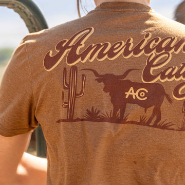 A person wearing the American Cattle Co Shadowhorn Tee, featuring "American Cattle" and a cactus with a longhorn silhouette marked "AC" on the back—ideal for those who live by the cattleman's code.