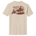 The Stampede Tee by American Cattle Co is beige, made from a soft cotton blend, and features a brown cowboy-on-bull graphic with cacti, desert scene, and the text 