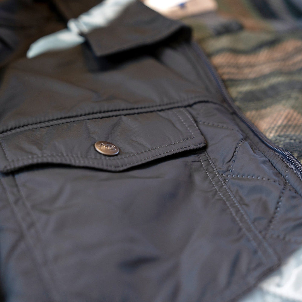 Snap-flap chest pocket on the quilted shell of the Sunday Jacket in Thundercloud, with patterned fleece lining visible.