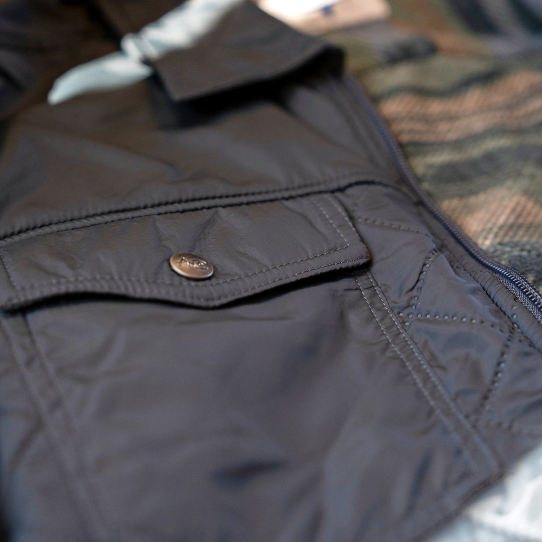 Snap-flap chest pocket on the quilted shell of the Sunday Jacket in Thundercloud, with patterned fleece lining visible.