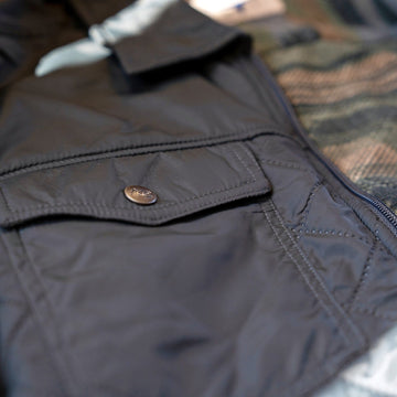 Snap-flap chest pocket on the quilted shell of the Sunday Jacket in Thundercloud, with patterned fleece lining visible.