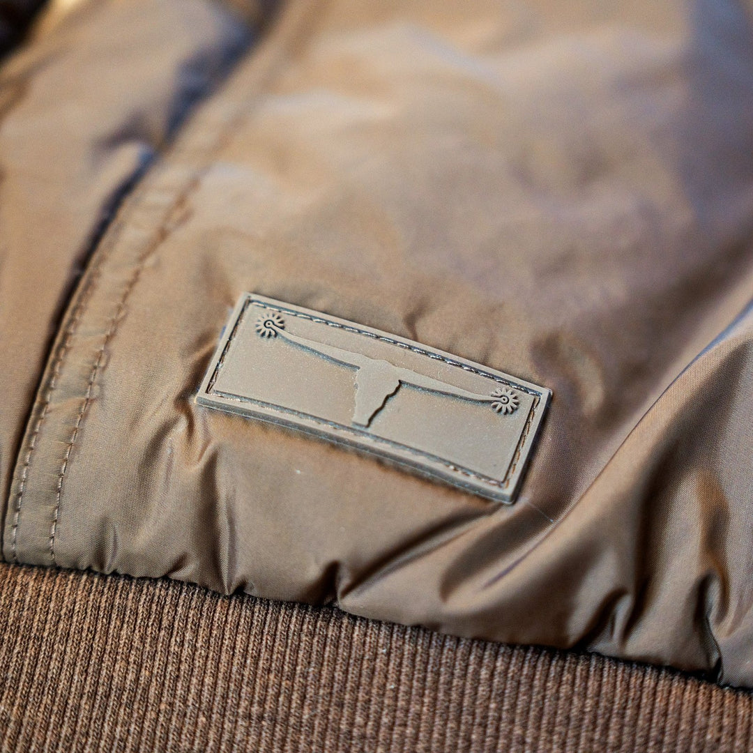 Close-up of the longhorn logo patch and ribbed waistband on The Cold Snap Puffer in Cocoa.
