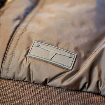 Close-up of the longhorn logo patch and ribbed waistband on The Cold Snap Puffer in Cocoa.