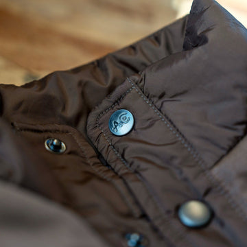 High stand collar with AC logo snap on The Cold Snap Puffer in Cocoa.