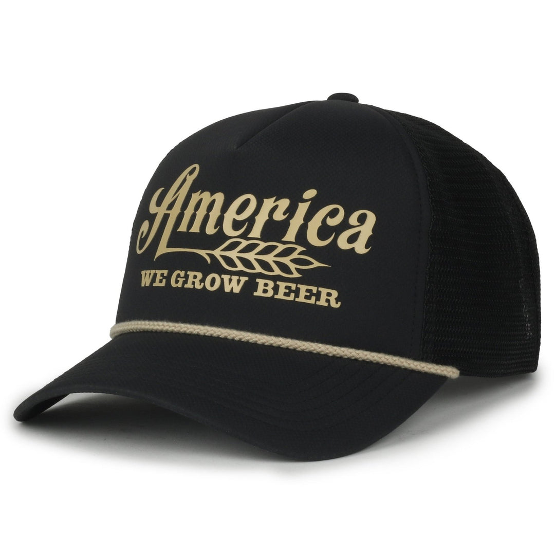 The We Grow Beer Foamie by American Cattle Co is a black mesh snapback hat featuring a mesh back and white rope detail above the brim. The front showcases "America" in a stylized font alongside a wheat graphic, with the phrase "WE GROW BEER" boldly displayed below, embodying the spirit of rural American pride.
