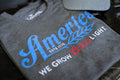A detailed view of the We Grow Coors Light Tee by Rural Cloth showcases a grey T-shirt adorned with bold blue and red text stating 