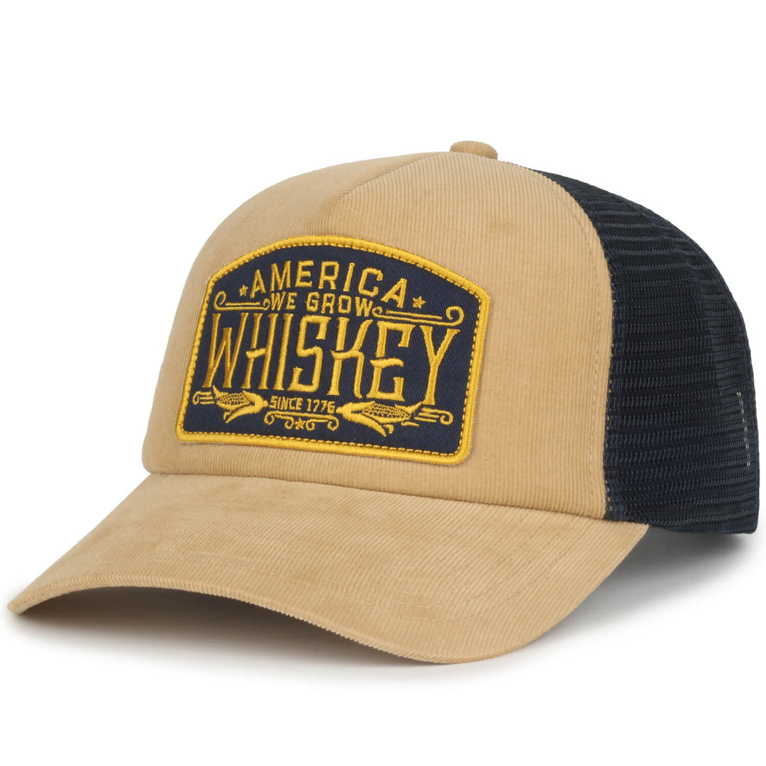 The We Grow Whiskey Hat-Corduroy by American Cattle Co is a tan and black cap with a yellow/black patch reading "America We Grow Whiskey Since 1776." It features corduroy front/brim, mesh back, and an adjustable snapback.