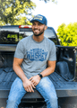 A man with a beard is sitting on the open tailgate of a black pickup truck. He is wearing the 