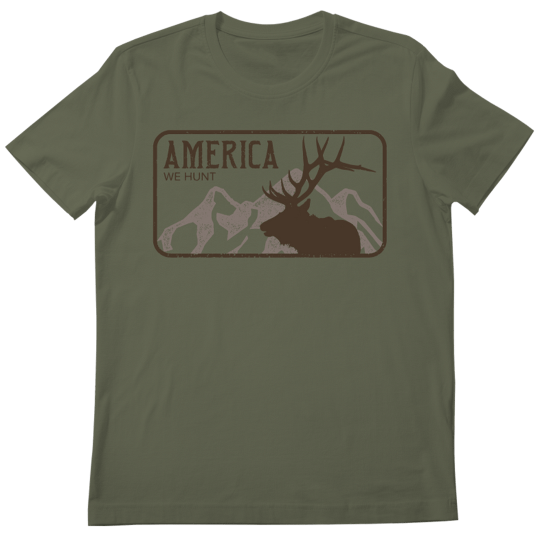 The America We Hunt Elk Tee-Military Green Frost by Rural Cloth features a deer silhouette, mountain backdrop, and bold “America We Hunt” text—perfect for outdoor enthusiasts and fans of elk hunting shirts.