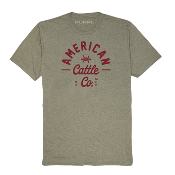 The Barb Tee by American Cattle Co is a heather gray short-sleeve t-shirt in a premium cotton blend, with bold red "American Cattle Co. TRD MRK" chest text and subtle "RURAL" detail inside the collar—a classic rancher style.