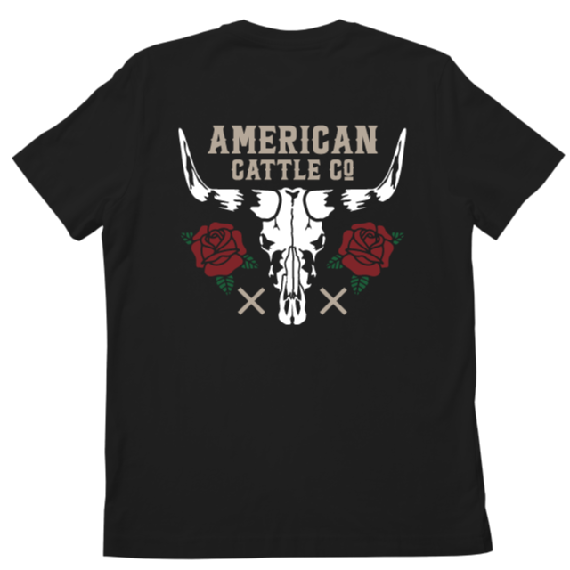 The image displays the back of a Skull & Roses Tee-Black by Rural Cloth, featuring a large bull skull flanked by two red roses and green leaves. Above the skull, bold text reads 
