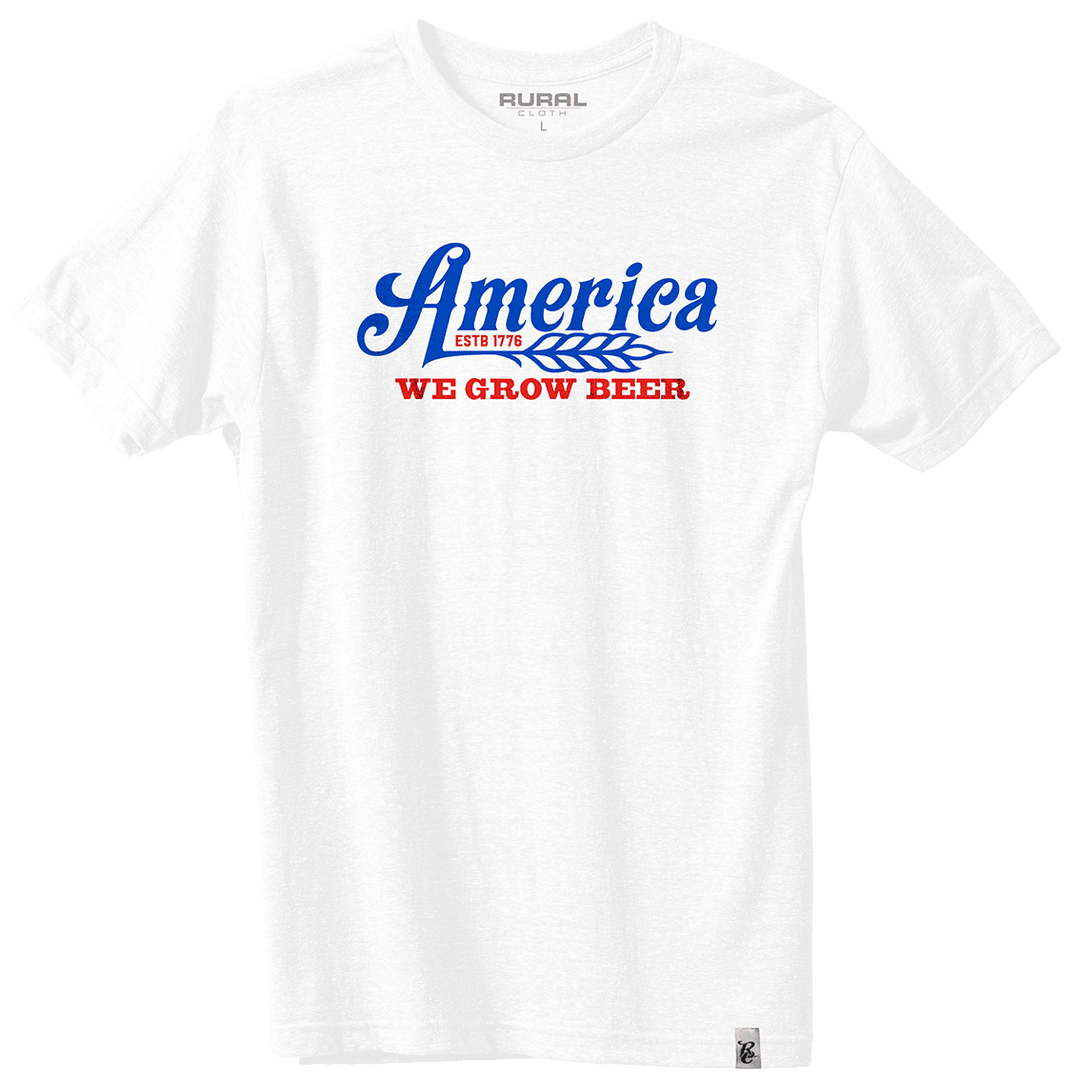 The We Grow Beer Tee - White by Rural Cloth features "America" in blue script, a wheat graphic, "ESTD 1776" in red, and bold "WE GROW BEER" text—all on premium weight fabric in an athletic modern fit.