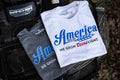 Two T-shirts lie on the front of an ATV. The left one is a gray 