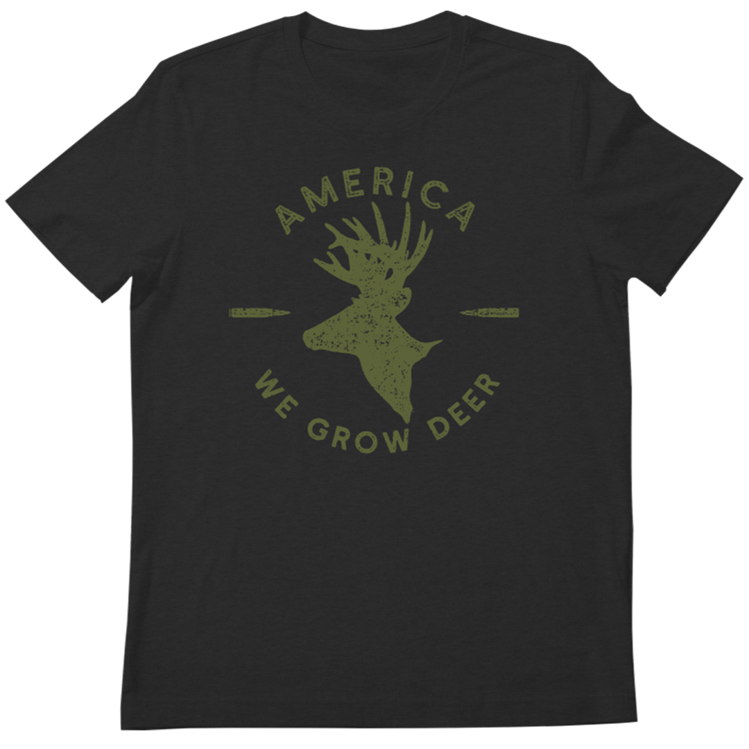 The American Cattle Co We Grow Deer Tee-Black features a green deer head silhouette, two horizontal arrows, and "AMERICA WE GROW DEER" text—celebrating deer conservation and wildlife stewardship.